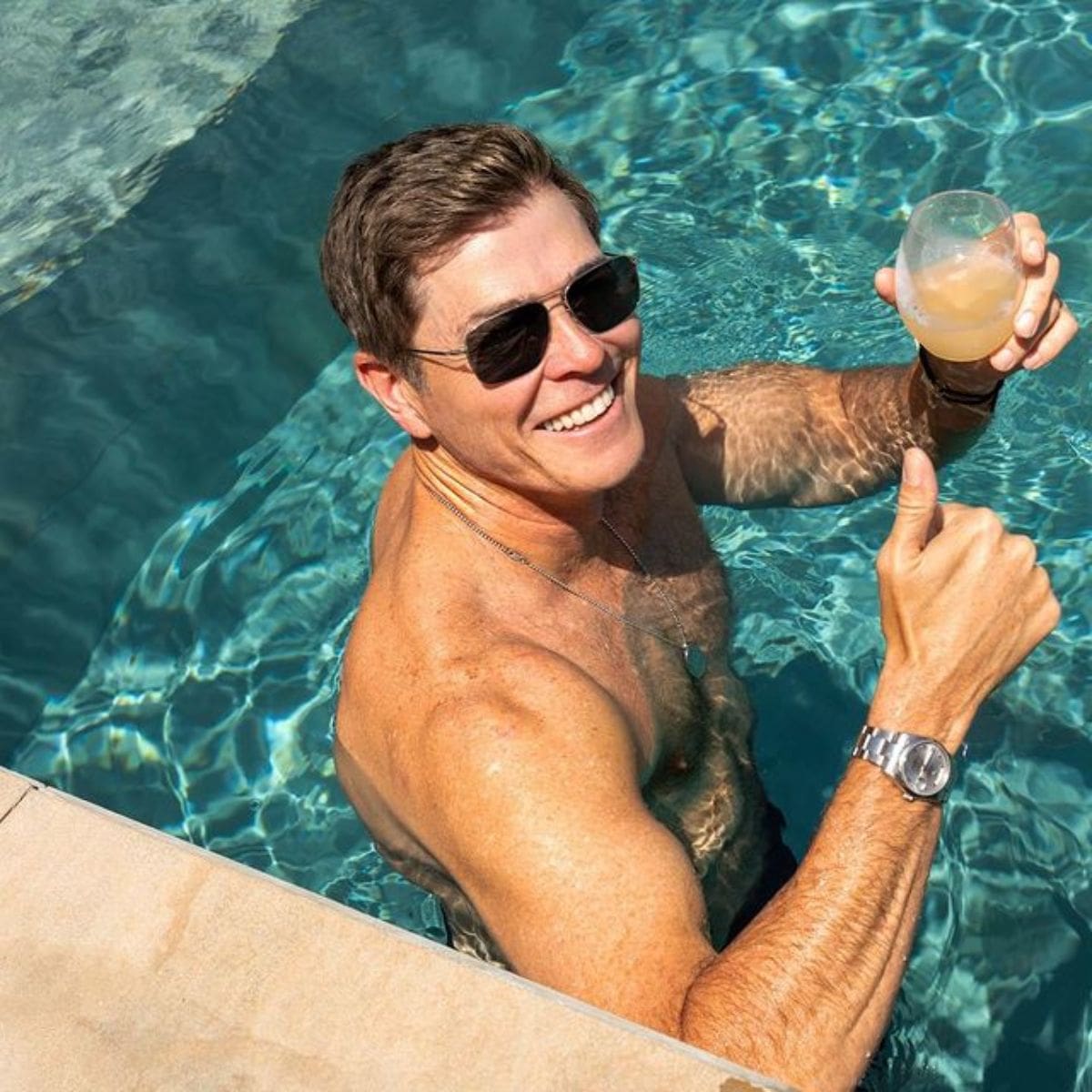 Patrick Whitesell posing for a photo shoot while holding a drink in the swimming pool.